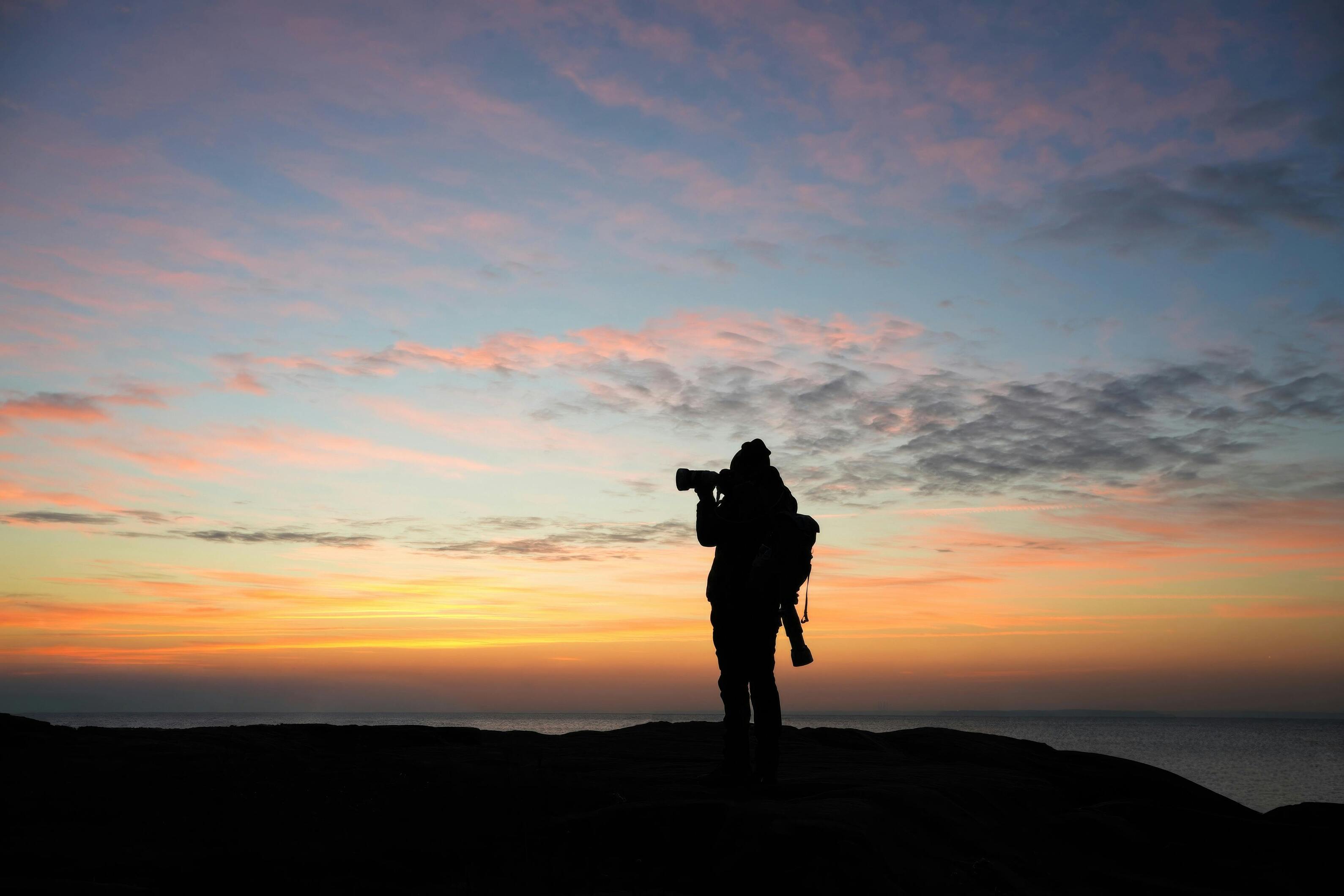 Silhouette of a photographer capturing a sunset scene with a camera.